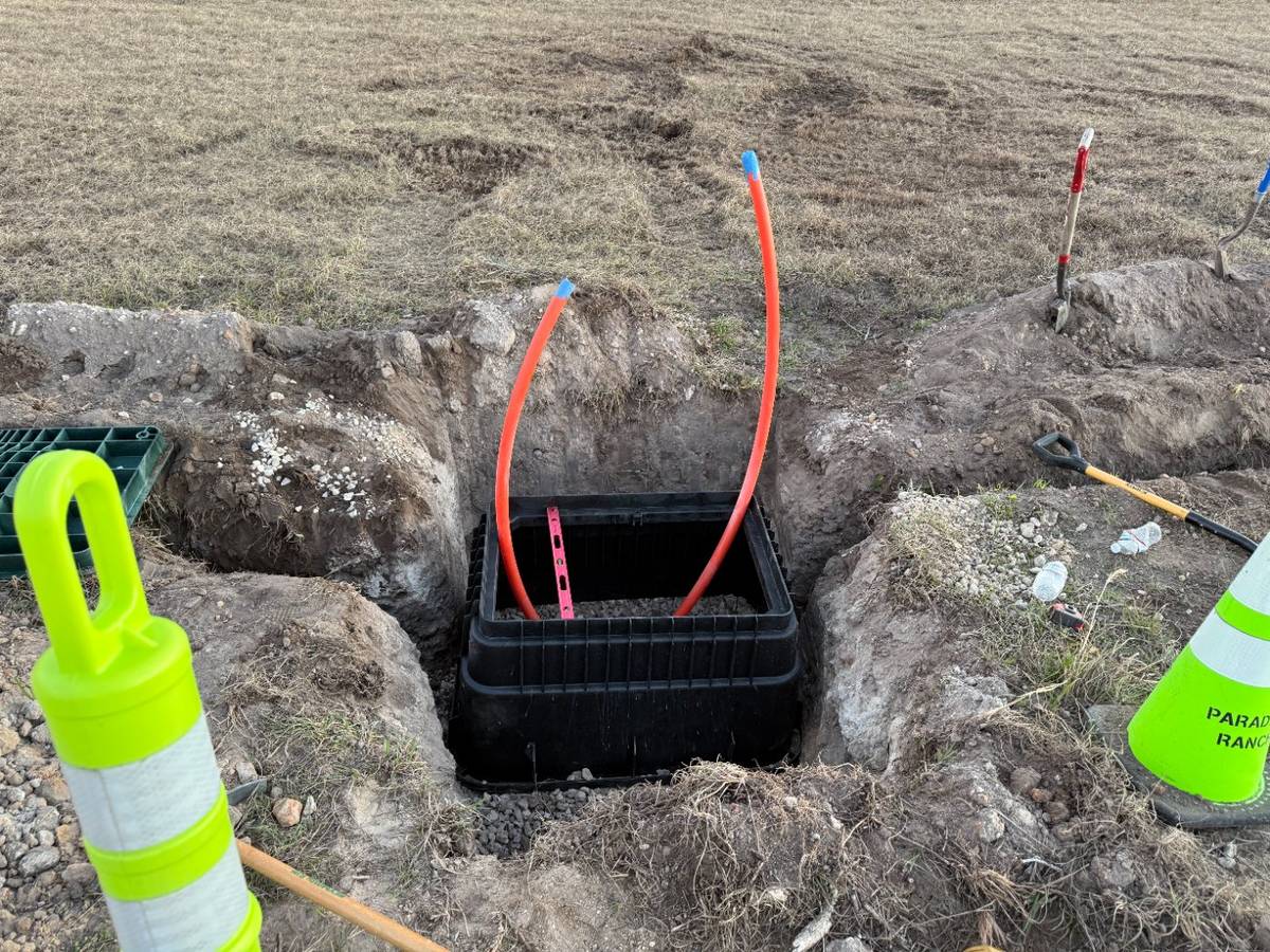 A fiber handhole set in a trench on a campus run, two orange conduits rising out of it