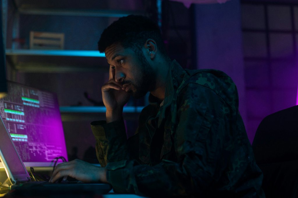 Analyst in a camouflage uniform working at a laptop in a dim room