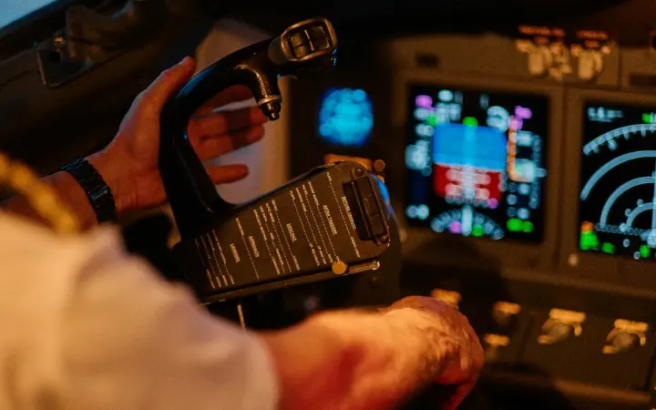 A pilot's hand on the throttle in a lit cockpit