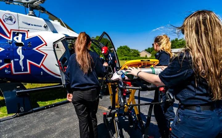 A flight crew wheels a stretcher to an air ambulance marked with the star of life, the work a hospital network supports