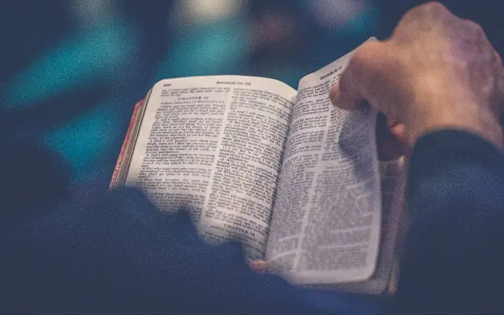 Hands holding an open Bible in low light