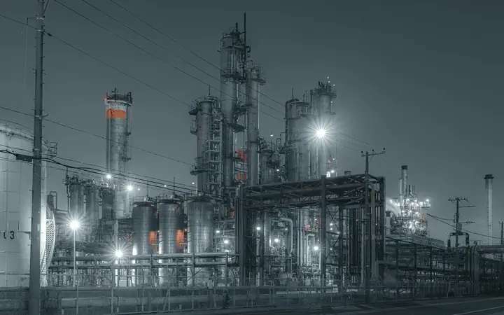A refinery lit at night, the plant floor an OT network reaches