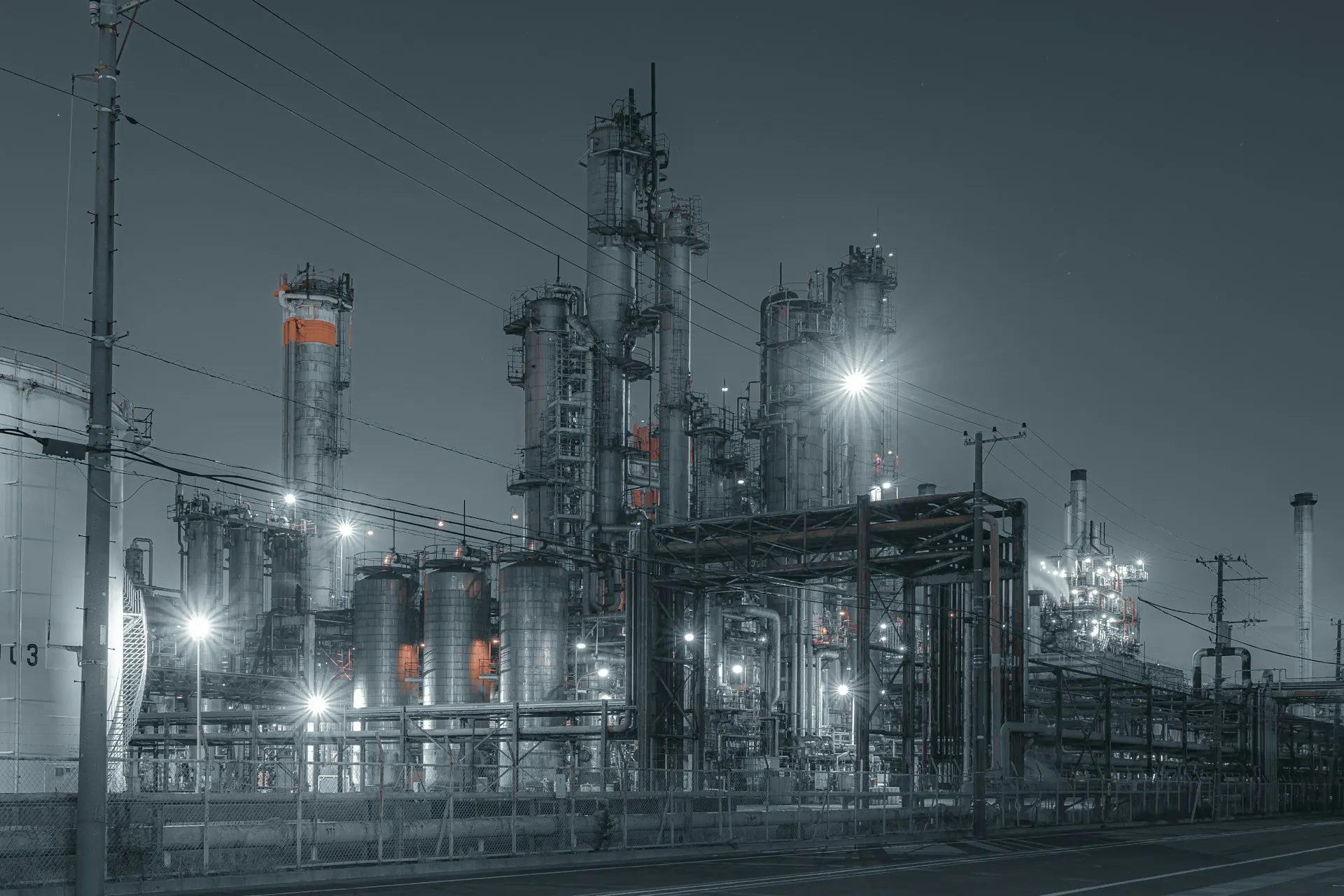 Petrochemical plant at night: distillation towers, tanks and pipe racks under floodlights