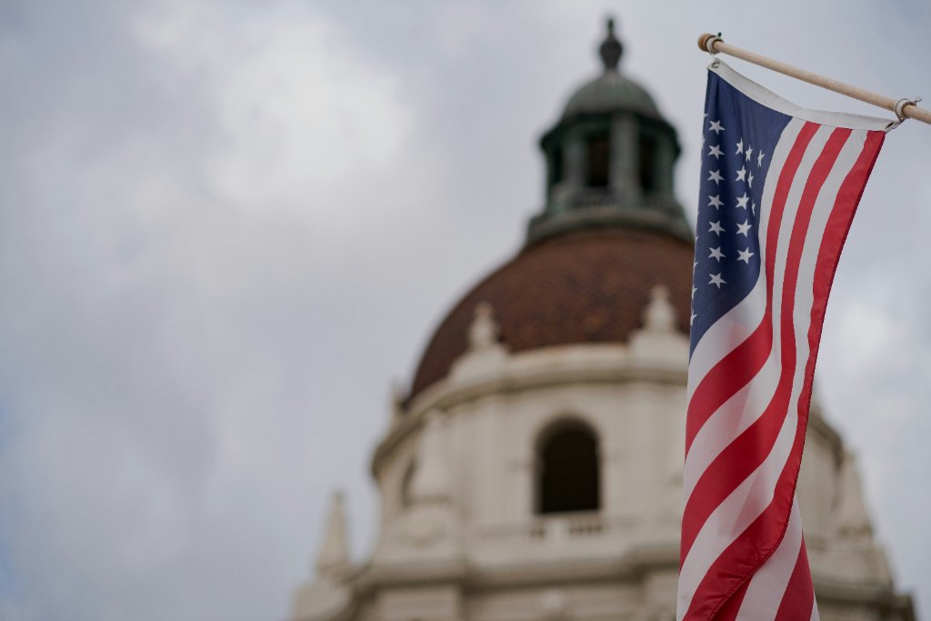 U.S. flag flying in front of a city hall dome under an overcast sky